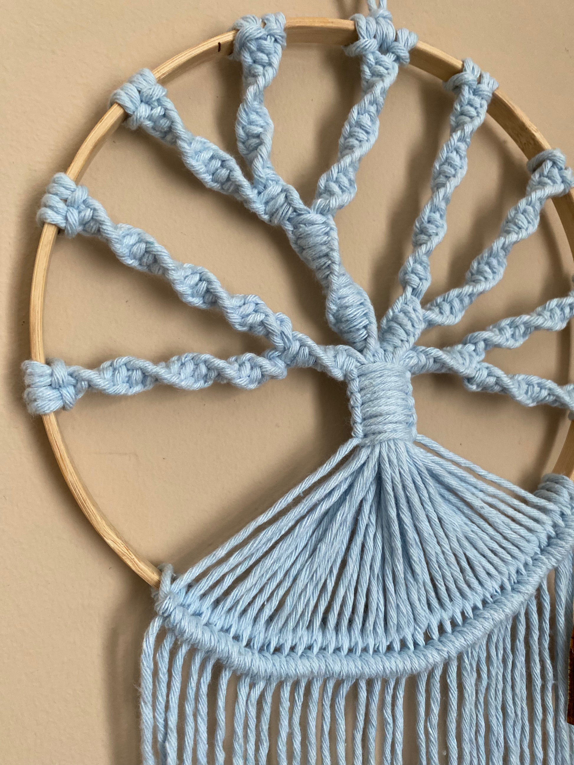 A close up image of a macrame tree of life wall hanging made on a circular wooden hoop with light blue knotted yarn.