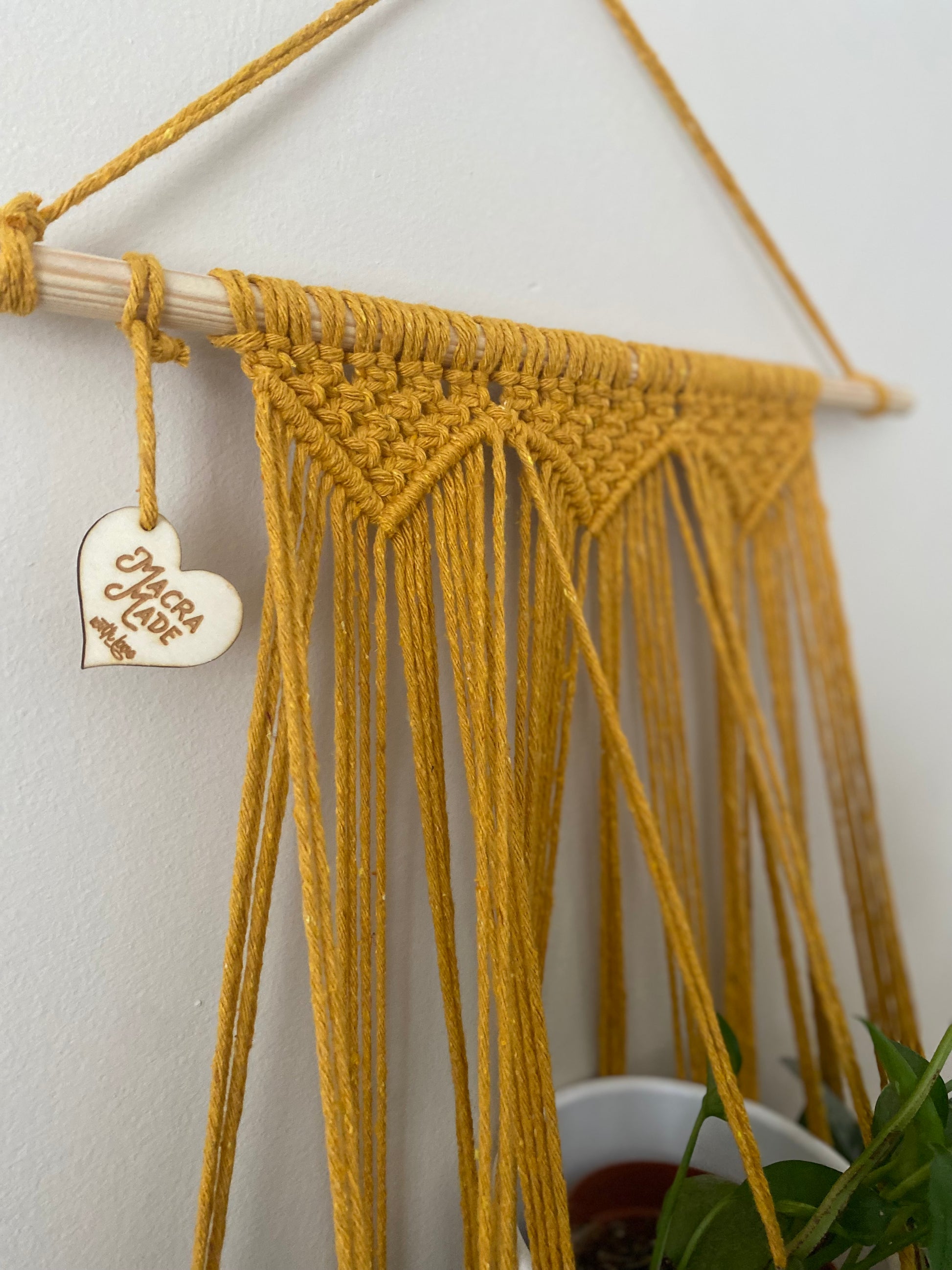Close up of the knotted section on a wall hanging macrame plant hanger, made with mustard yellow cotton on a long wooden dowel.
