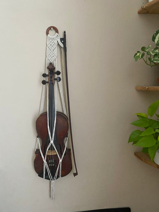 A dark wooden violin hanging in a macrame wall hanger, made with natural off white coloured recycled cotton on a wooden ring.
