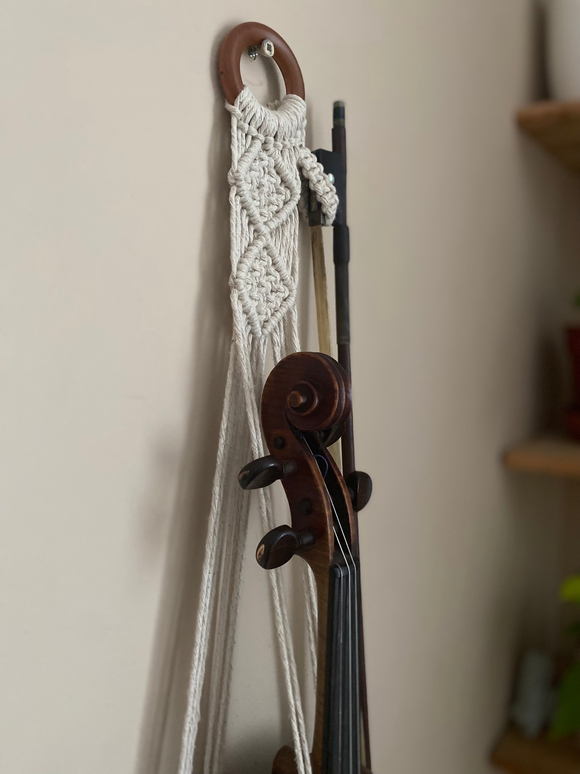 A dark wooden violin and bow hanging in a macrame wall hanger, made with natural off white coloured recycled cotton on a wooden ring.