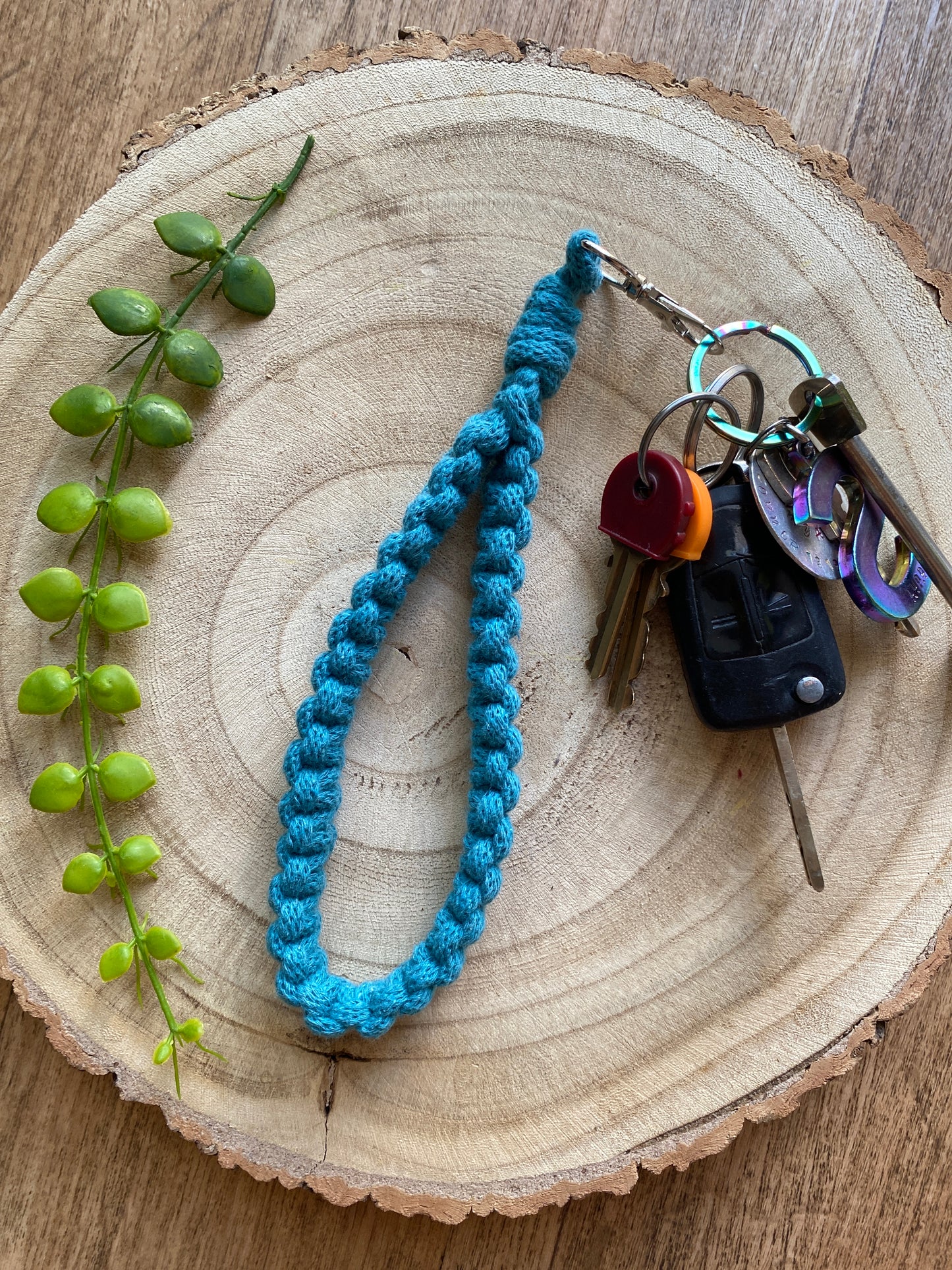 Handmade macrame wristlet keychain with metal clasp, made with teal blue recycled cotton. Shown attached to a small set of car keys.