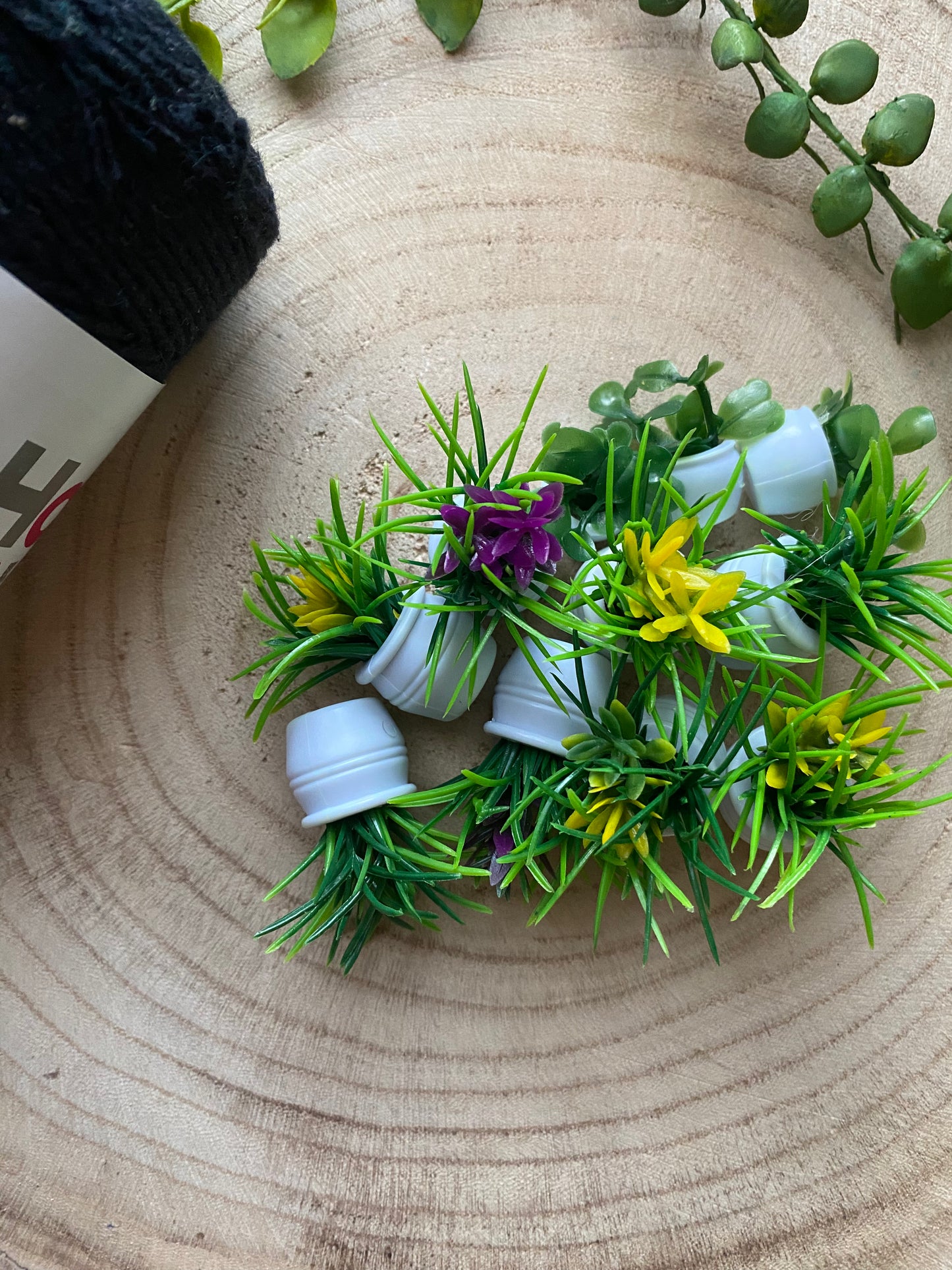 A small selection of mini artificial plants of various shapes and colours, laid together on a wooden surface next to a skein of black yarn.