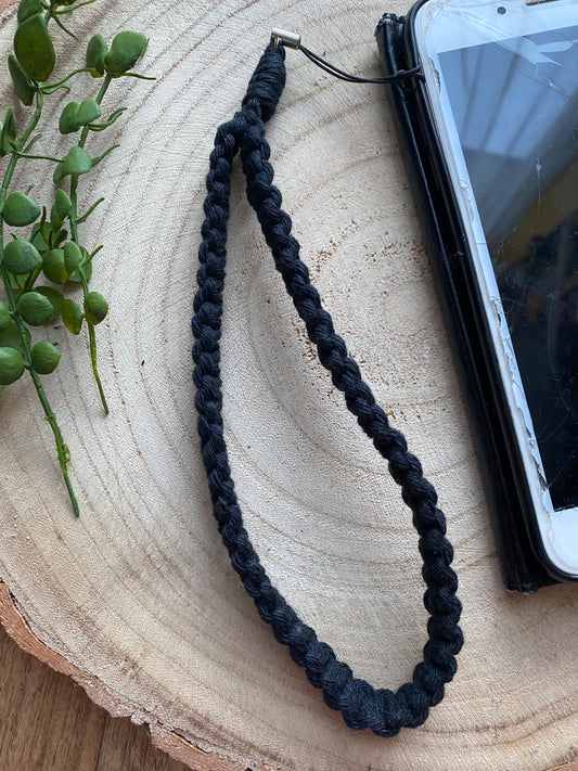 Handmade macrame phone wristlet strap in black recycled cotton, shown attached to an iPhone with a slightly cracked screen edge.