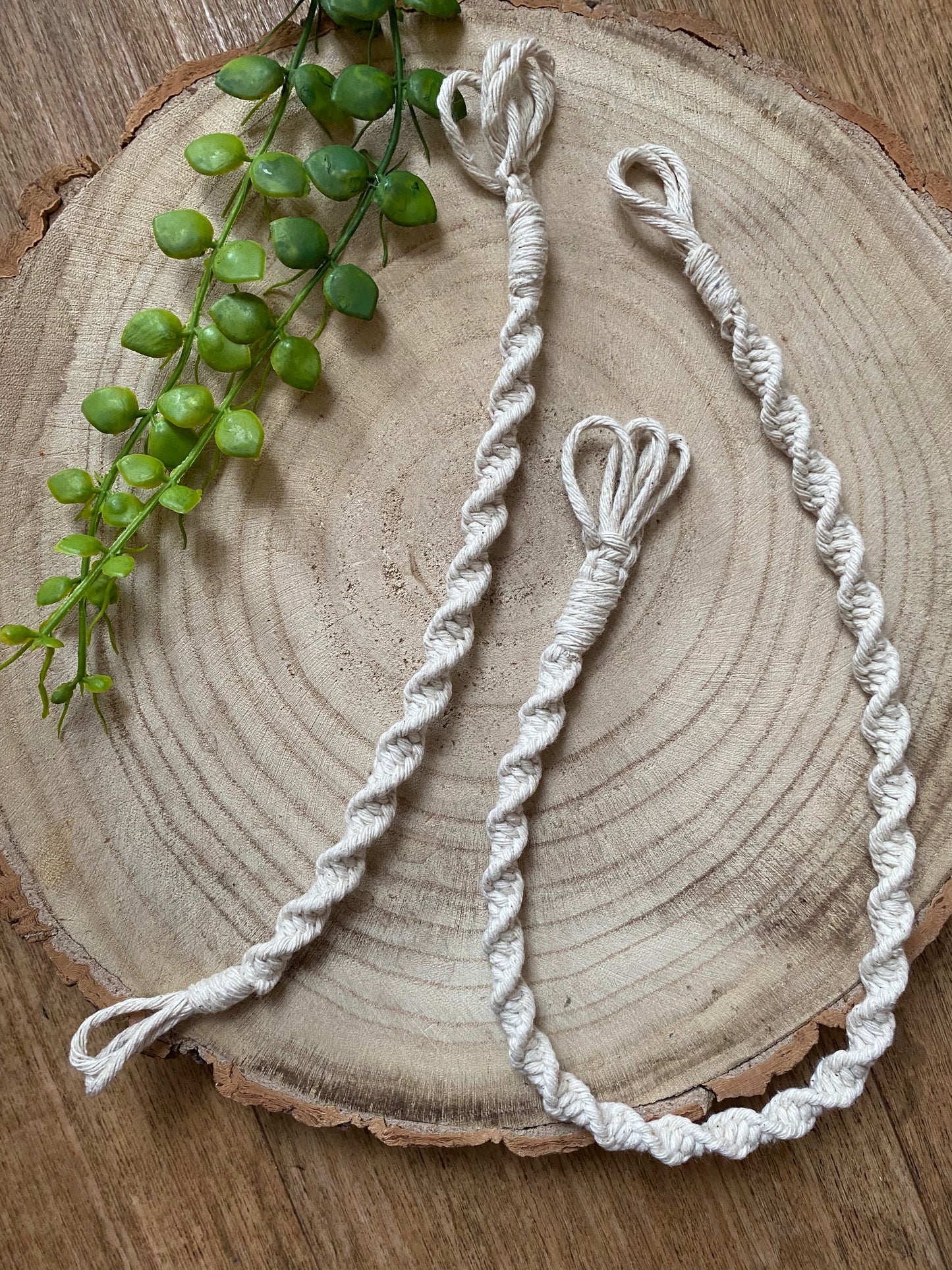 Two macrame plant hanger extensions of different lengths, each made with natural cotton yarn, laid out next to each other on a wooden surface.