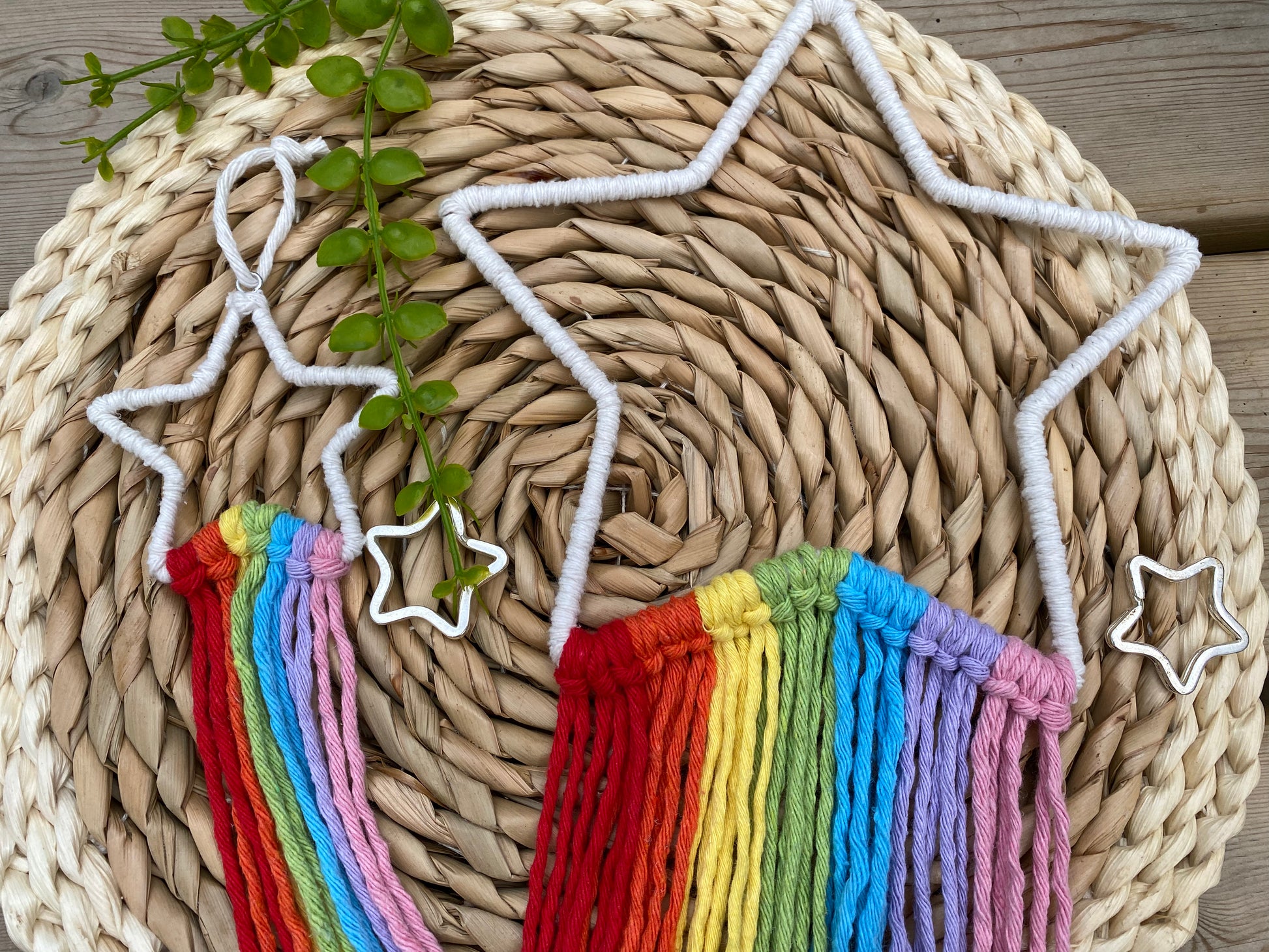 Two white star frames with rainbow hanging tassels, one small, one large, lay beside each other on a round wicker mat.
