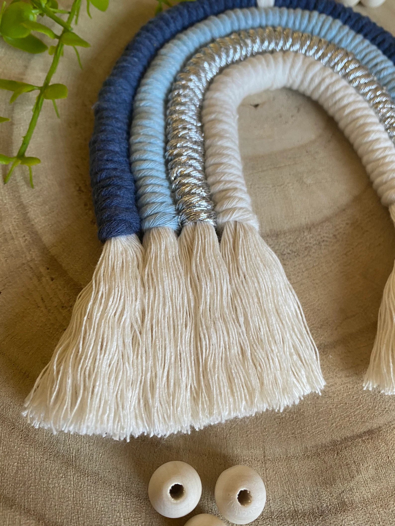 Close up view of a handmade blue macramé rainbow wall hanging made with soft cotton cords against a wooden background.