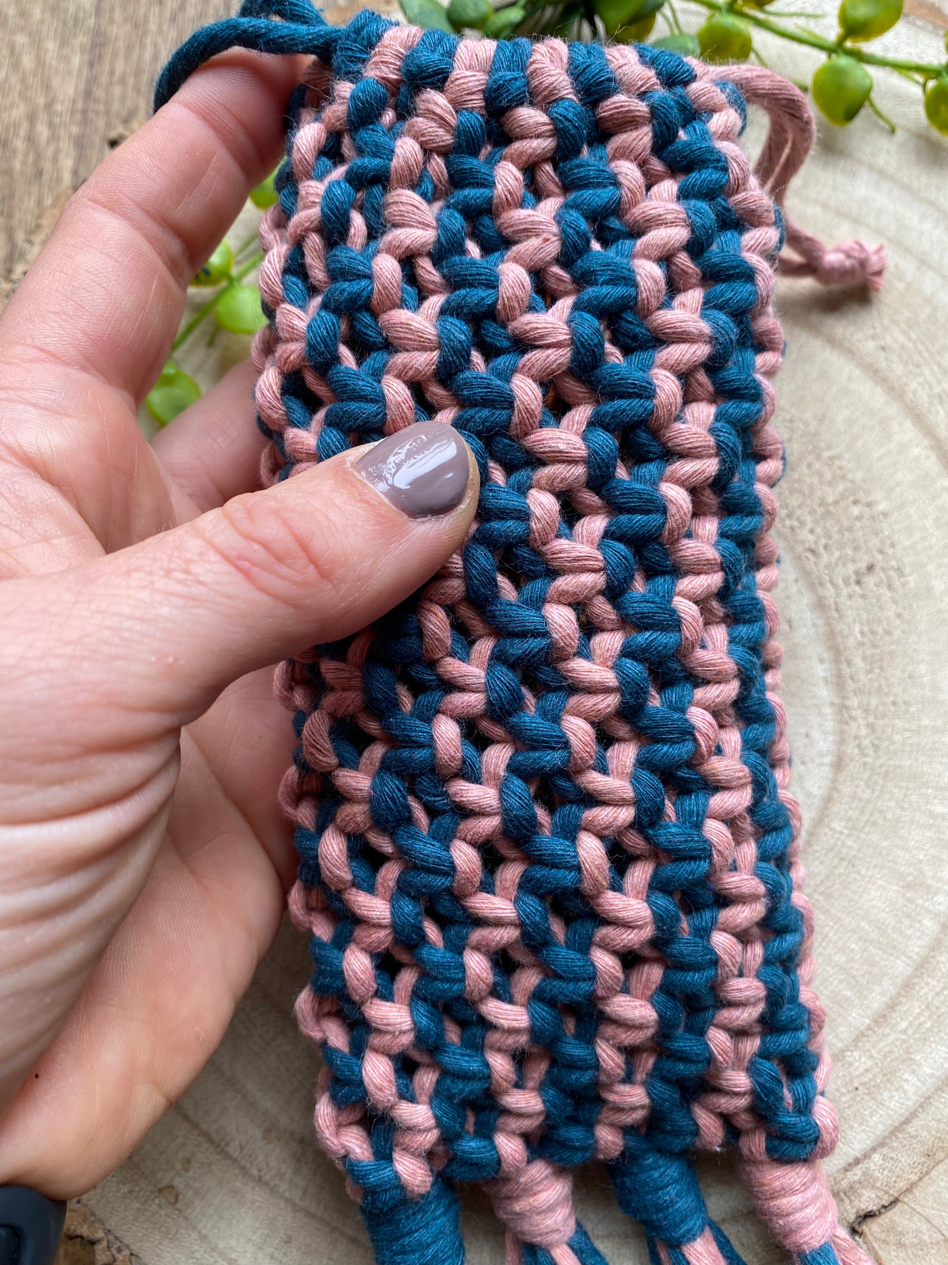 A hand holding a handmade macrame soft glasses pouch made with pink and blue cotton yarn.