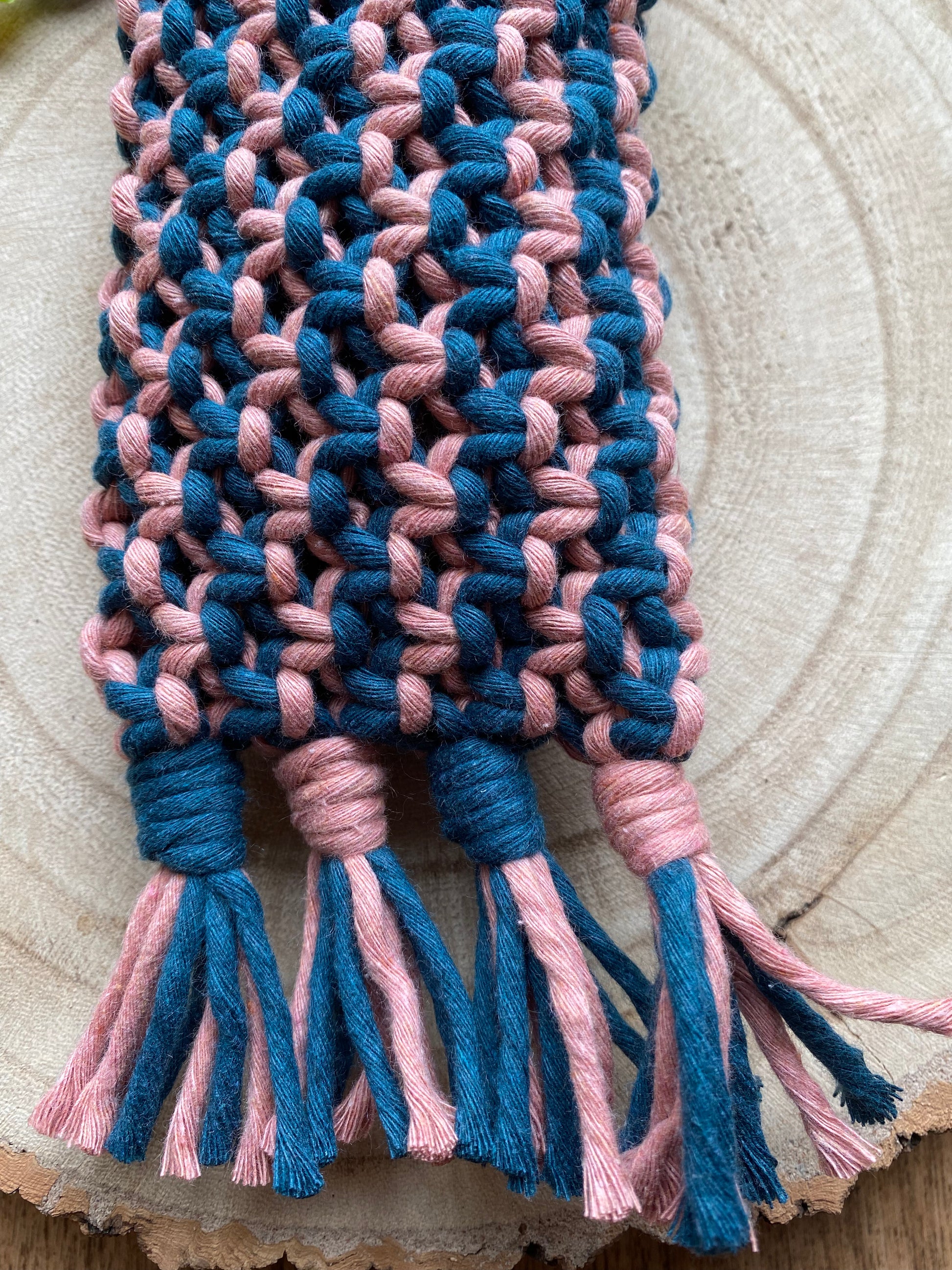 Close up details of intricate knots and tassels on a handmade macrame glasses pouch, made with pink and blue cotton yarn.