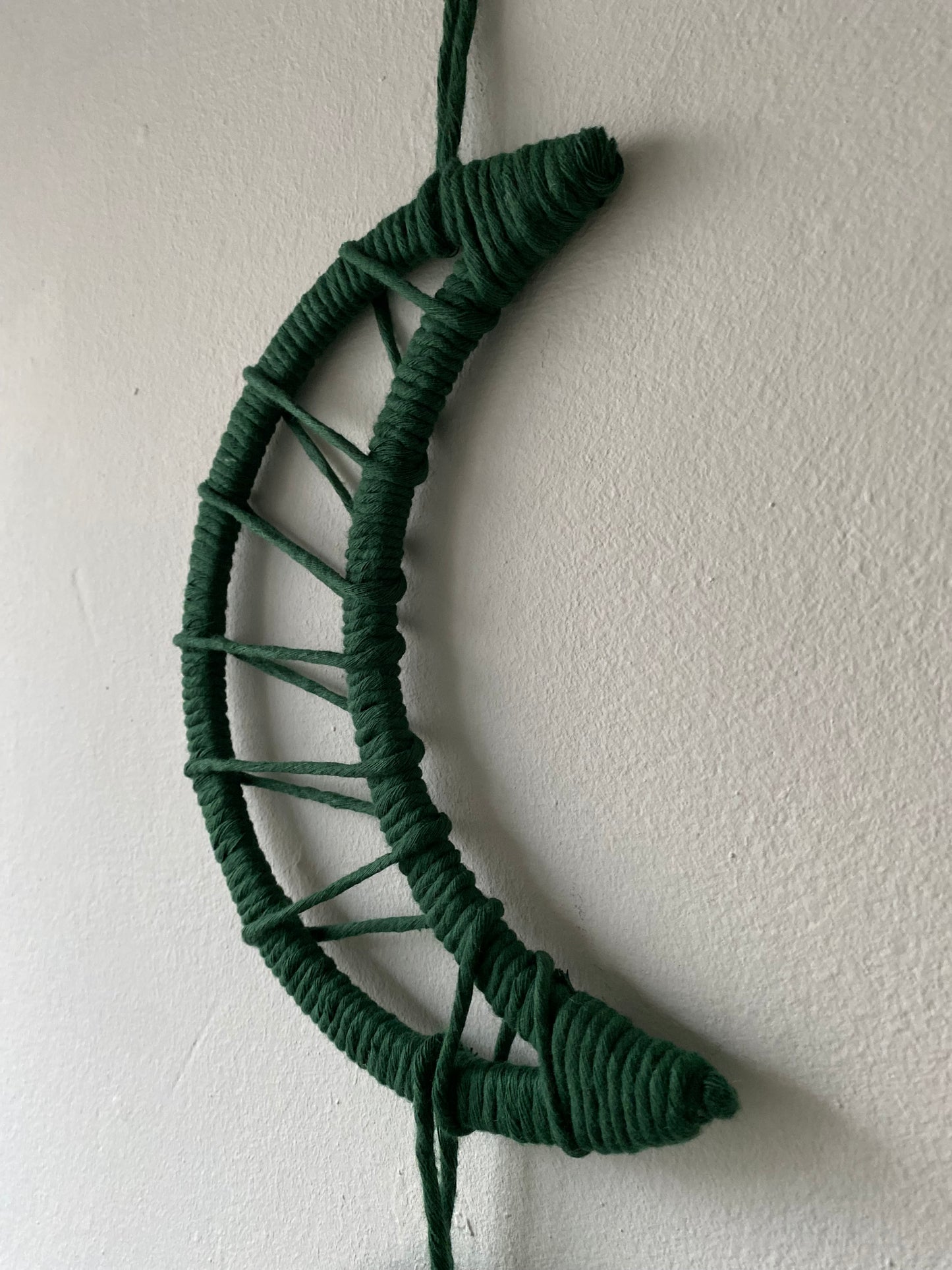 Close up of a macramé moon shaped wall hanging wrapped in dark green yarn.