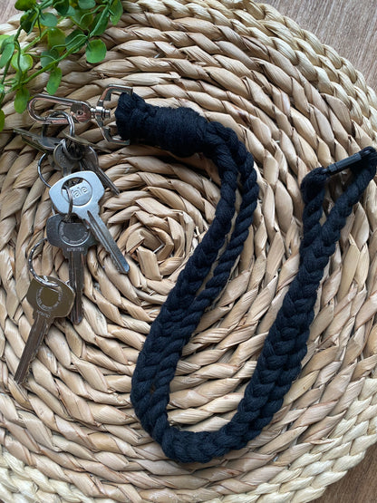 A set of keys attached to a Macra-Made-With-Love Eco friendly lanyard badge holder - 34” lies on a woven circular placemat. A small green plant is partially visible in the upper left corner.