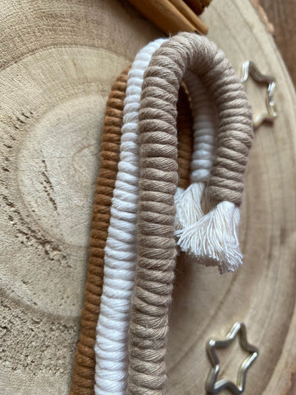 A close up of a set of three Christmas candy cane shaped macrame ornaments in beige, white, and brown colours with tassels, stacked on top of each other. 