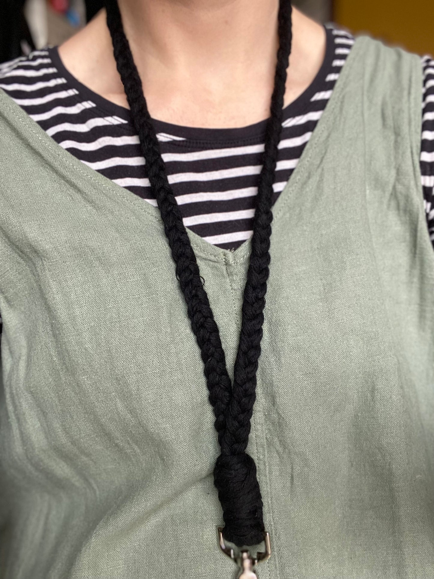 A person wearing a green sleeveless top over a black and white striped shirt, with a Macra-Made-With-Love Eco friendly lanyard badge holder - 34” around their neck. The bottom half of the lanyard, ending in an ID badge holder clasp, is visible in the photo.