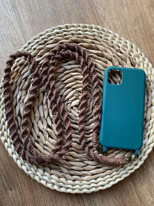 An empty green phone case with a long brown strap attached to the bottom of it with two clips, sits on a round wicker placemat on top of a wooden surface. 