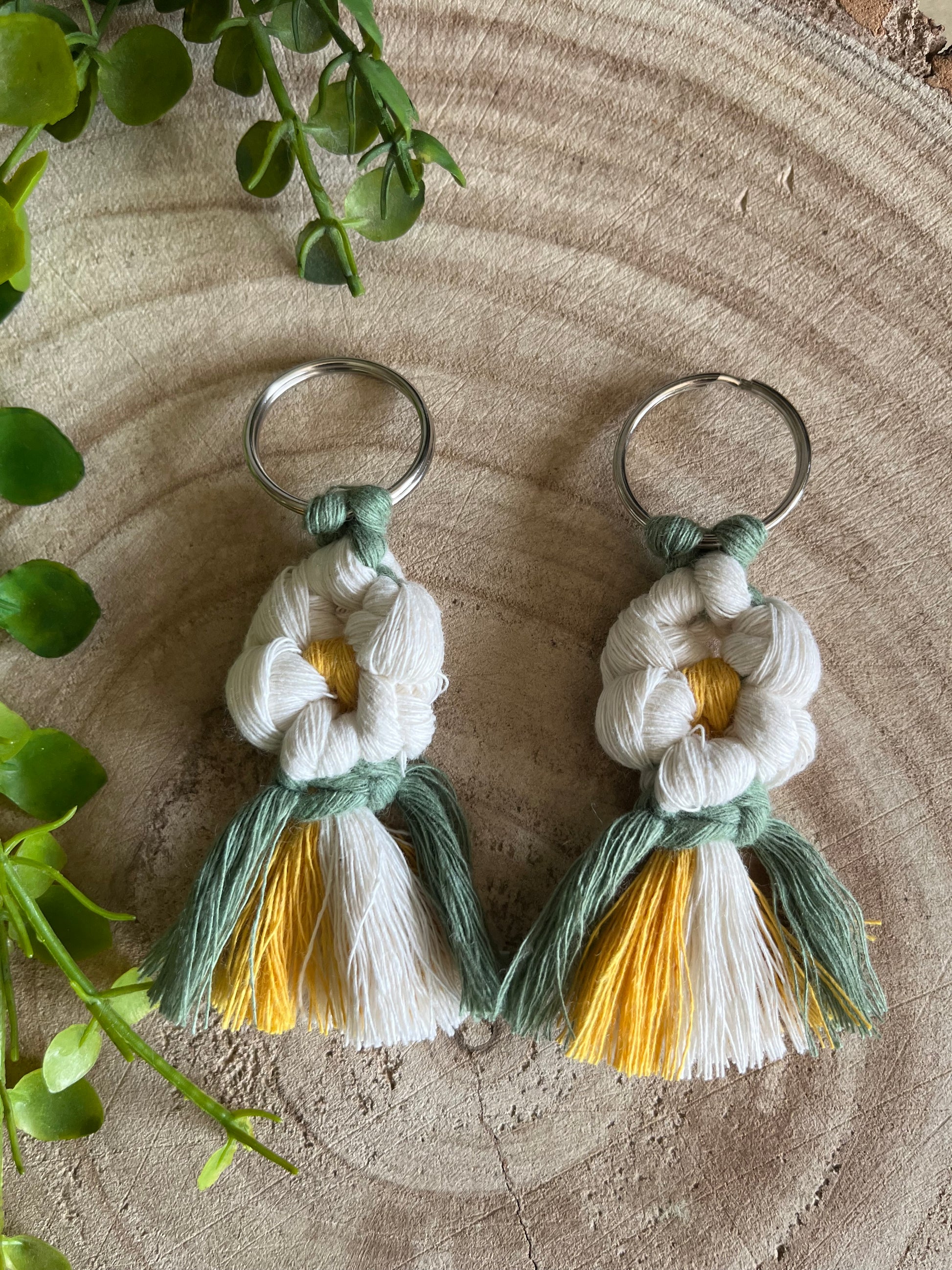 A pair of handmade macrame daisy boot charms, made with recycled cotton, on a wooden surface.