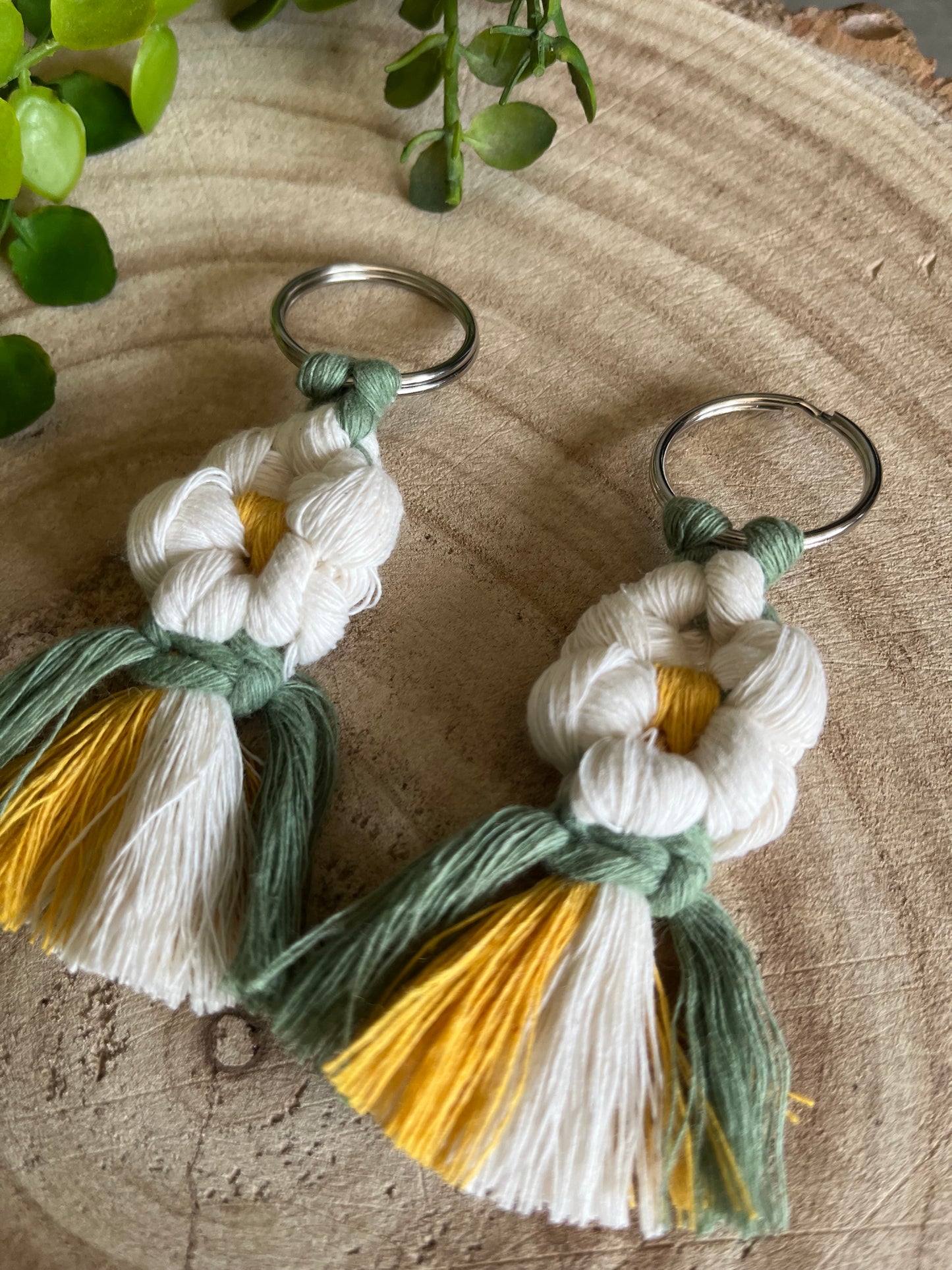 A pair of handmade macrame daisy boot charms, made with recycled cotton, on a wooden surface.