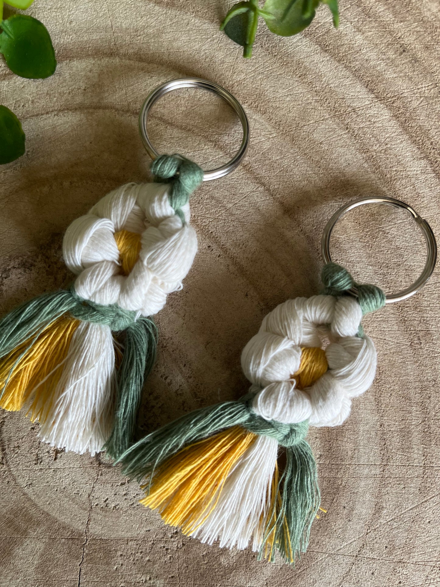 A pair of handmade macrame daisy boot charms, made with recycled cotton, on a wooden surface.