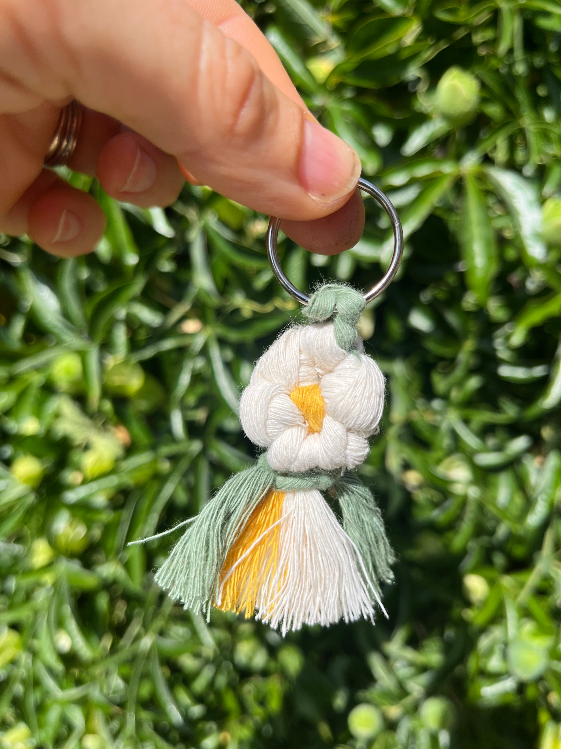 A hand holding a handmade macrame daisy boot charm, made with recycled cotton.