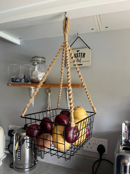Black metal basket hanging from a jute rope, holding red onions and white potatoes. 