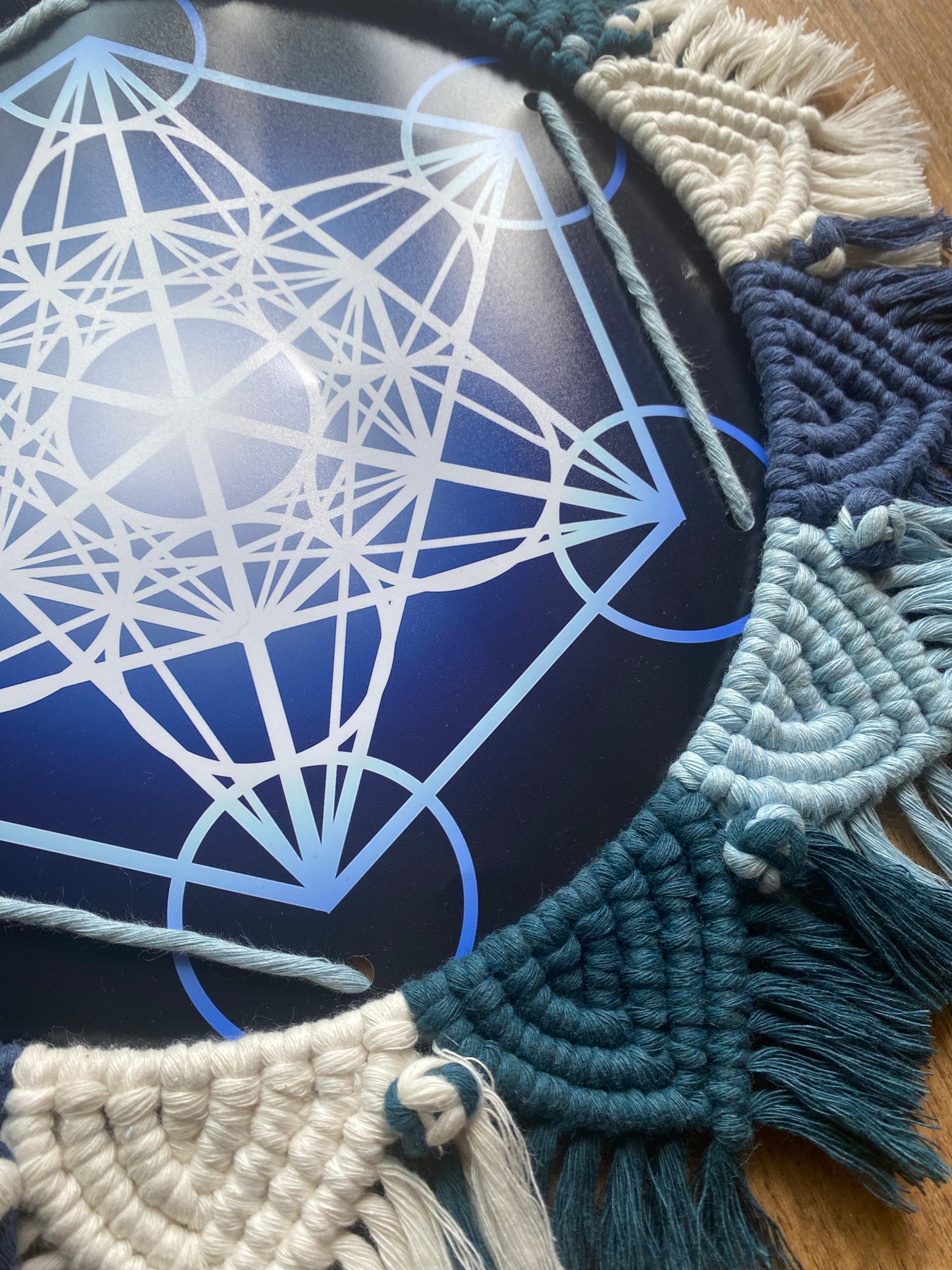 Close up of the intricate knots on a macrame mandala frame knotted with blue and white yarn, surrounding a Metatron’s Cube geometric print in the middle. 