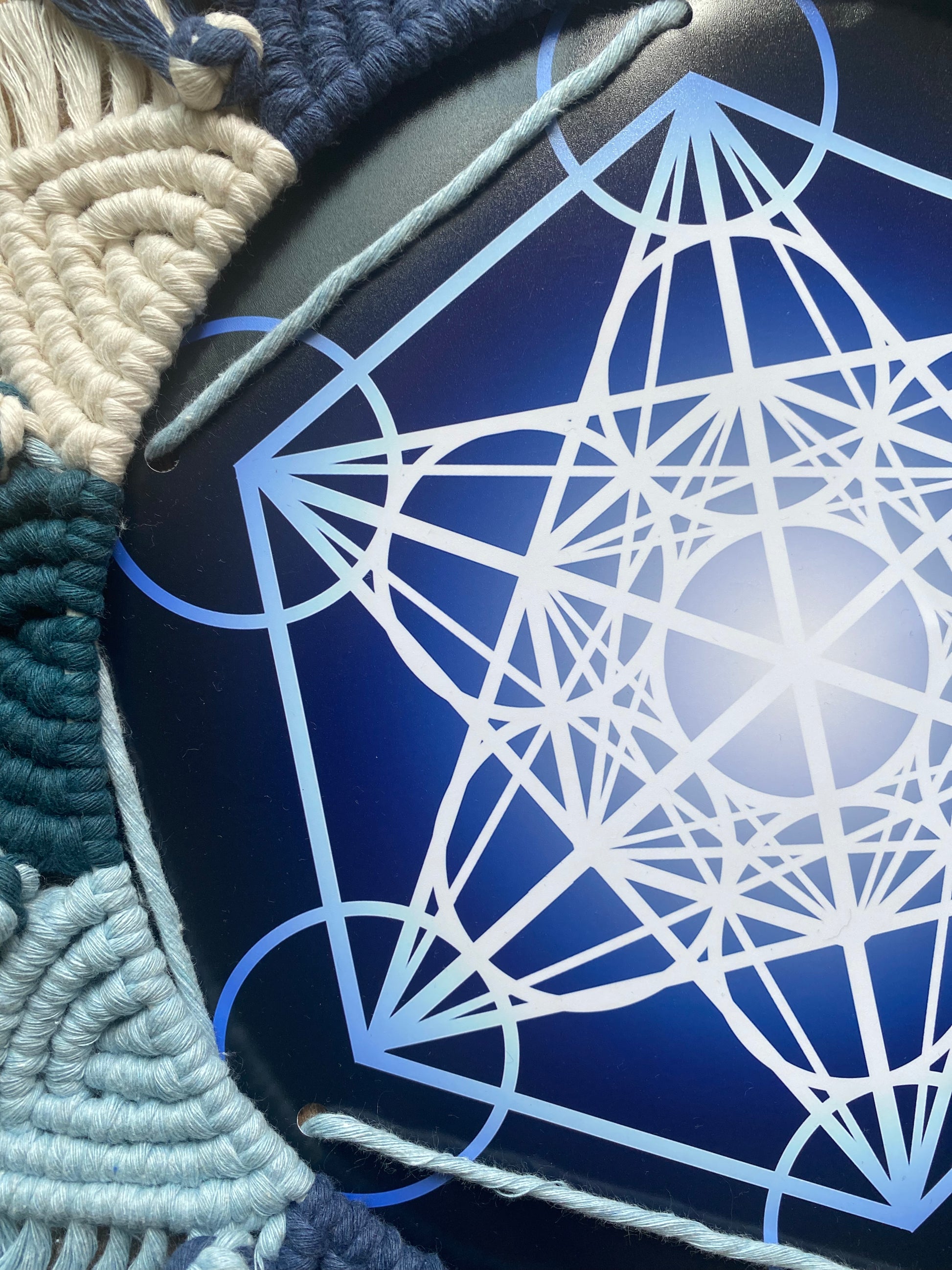 A blue and white Metatron’s Cube geometric print surrounded by an intricately knotted macrame mandala frame. 