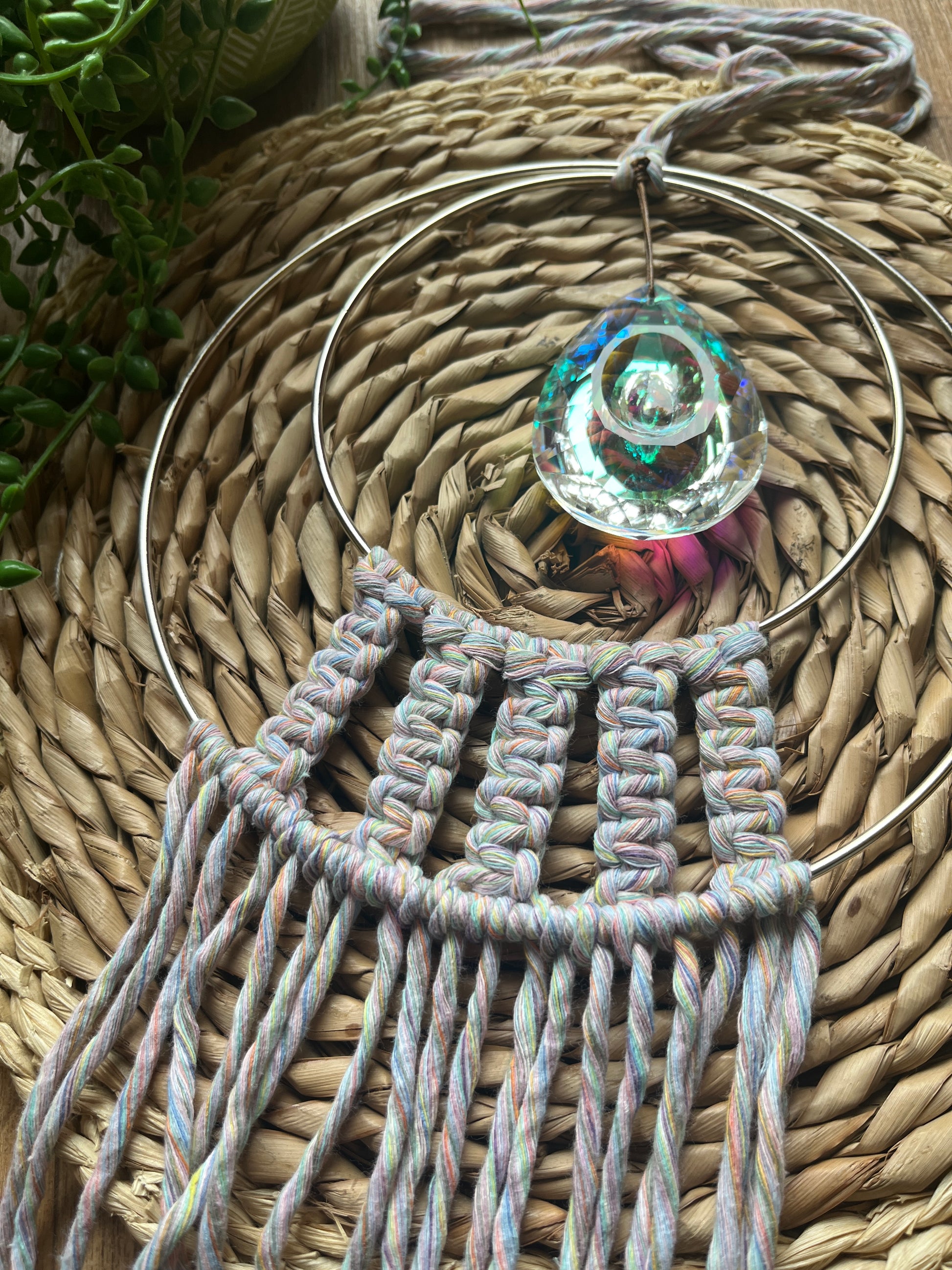 Close up of Handmade macrame Suncatcher made with pastel coloured recycled yarn, on two metal hoops, with a large hanging crystal in the centre. 
