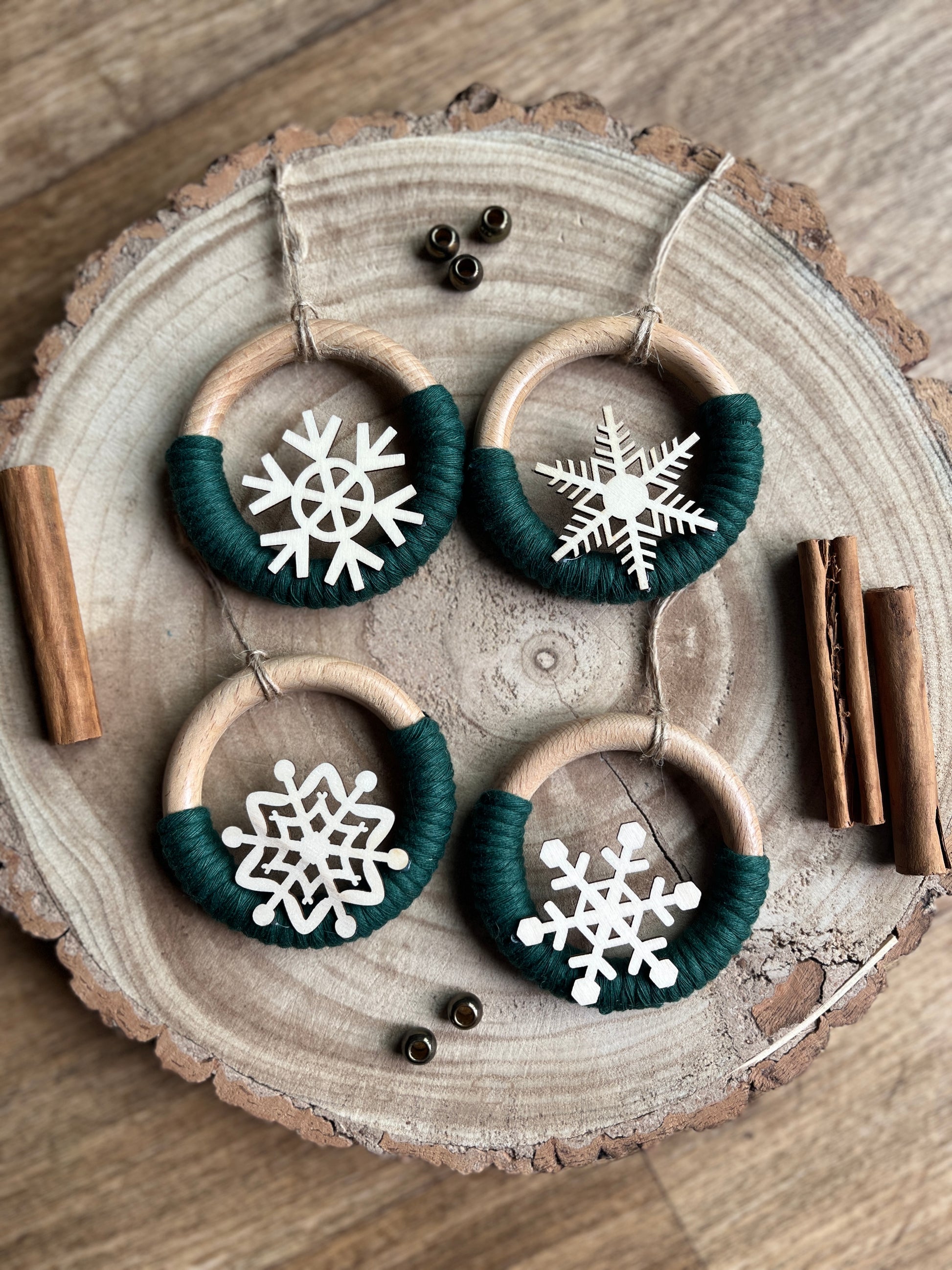 Decorative wooden ornaments, made on wooden rings with pine green yarn and finished with wooden snowflake designs, displayed on a rustic wooden surface.
