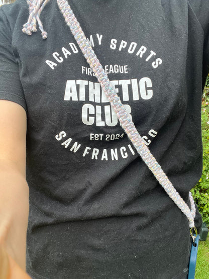 A woman stands outside wearing a black t shirt with white text on it, she has a crossbody phone strap across her body attached to a blue phone case. 