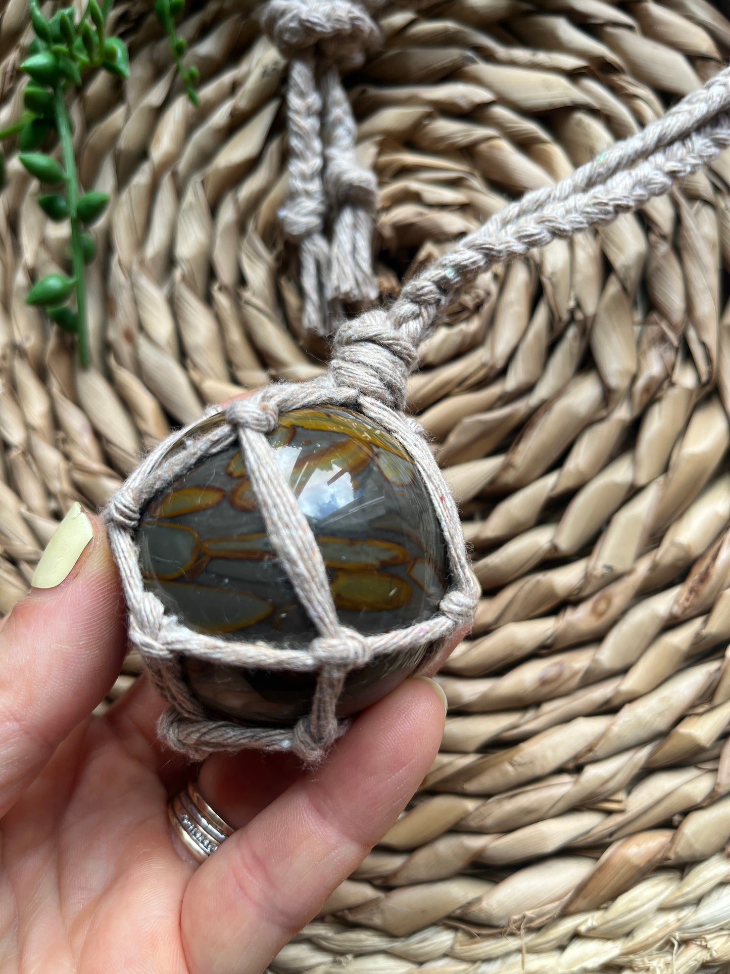 A hand holding a large bamboo jasper sphere held neatly inside a knotted macrame hanger made with taupe recycled cotton.