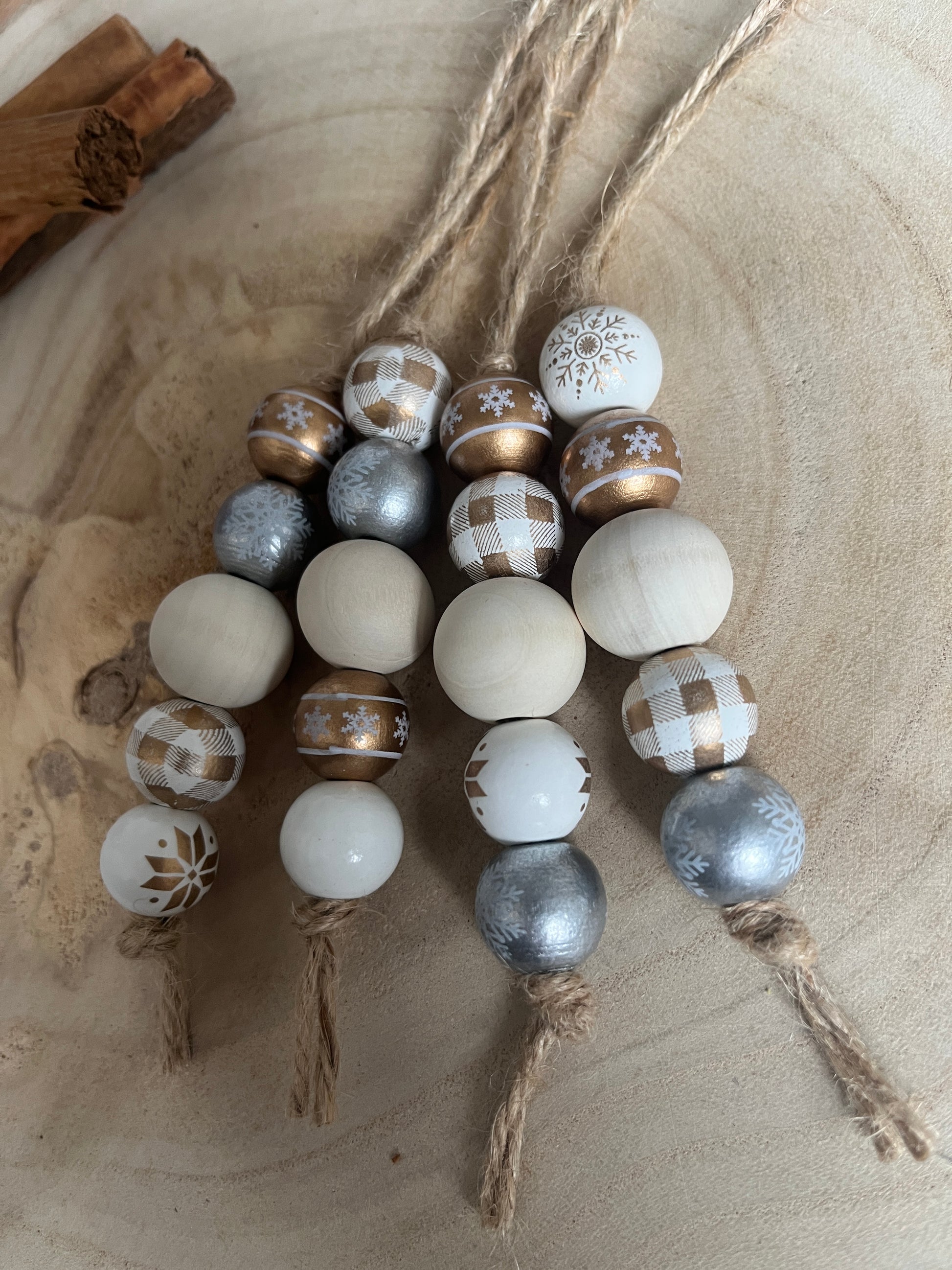 Decorative string of beads with white, gold, and silver patterns on a wooden surface.