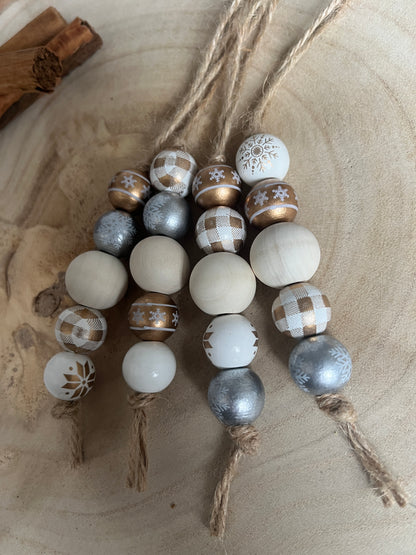 Decorative string of beads with white, gold, and silver patterns on a wooden surface.
