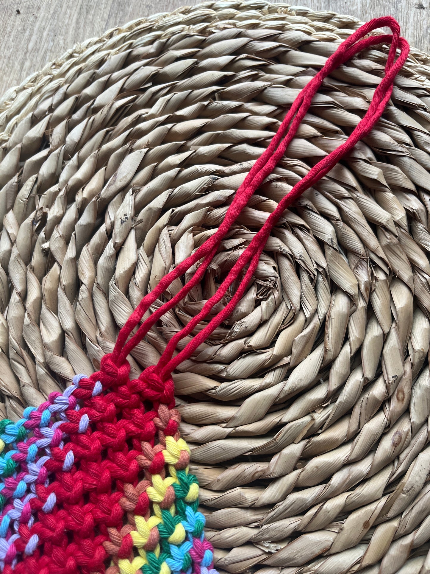 Colourful knotted pouch with long red hanging cord, on a woven mat