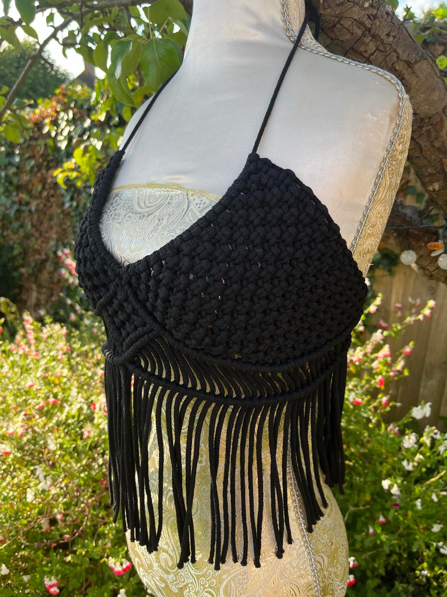 Black macrame halter top with fringe on a mannequin against a garden background