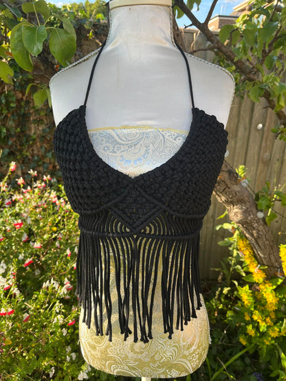 Black macrame halter top with fringe on a mannequin against a garden background
