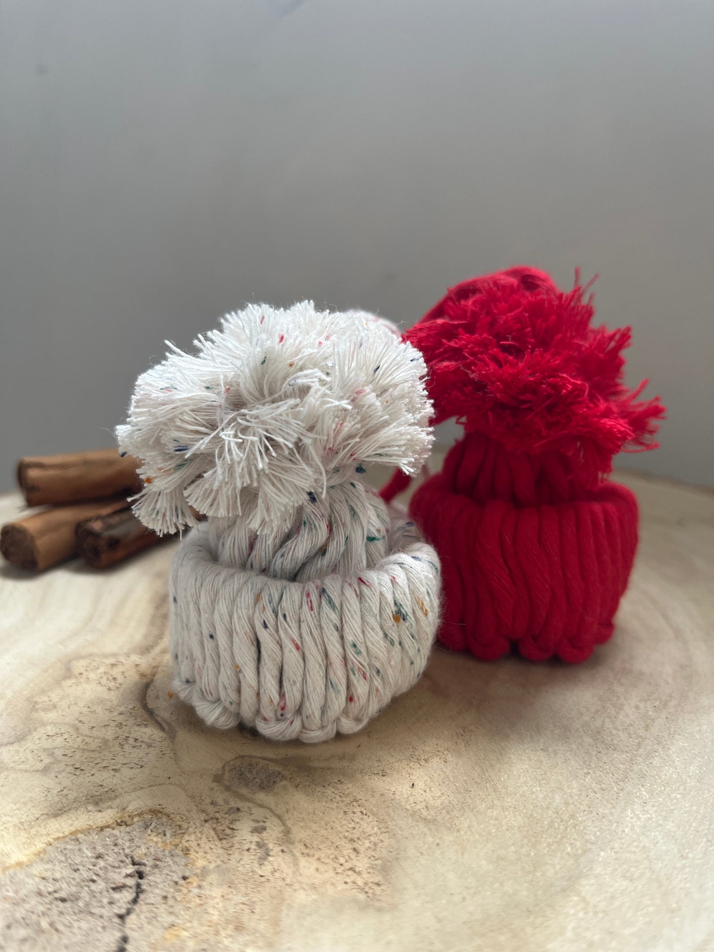 Red and white pom-pom hat ornaments with cinnamon sticks on a textured surface