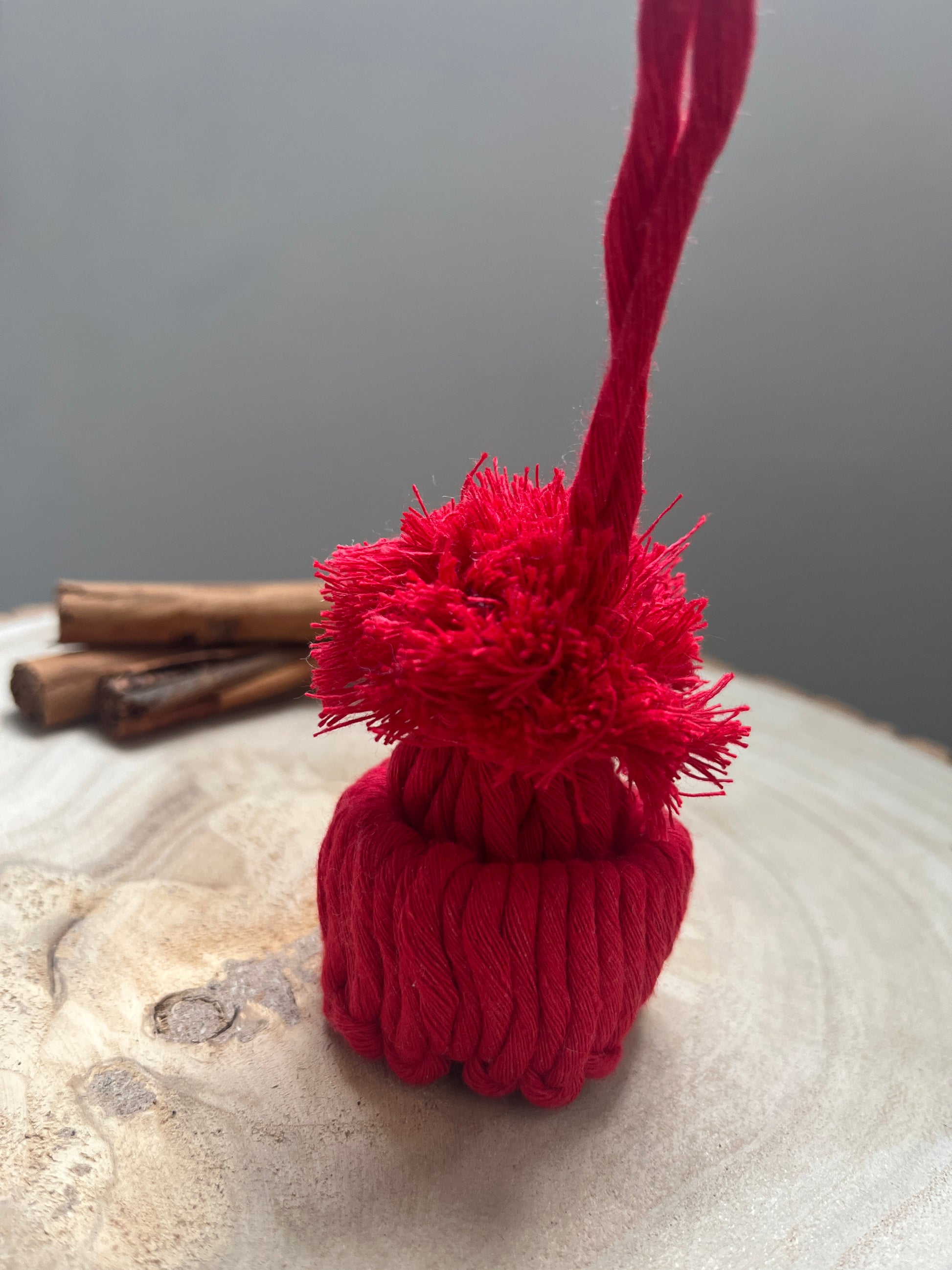 Close up of a mini pom pom hat ornament made with red yarn, on a wooden surface
