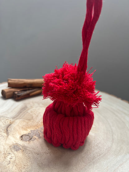 Close up of a mini pom pom hat ornament made with red yarn, on a wooden surface