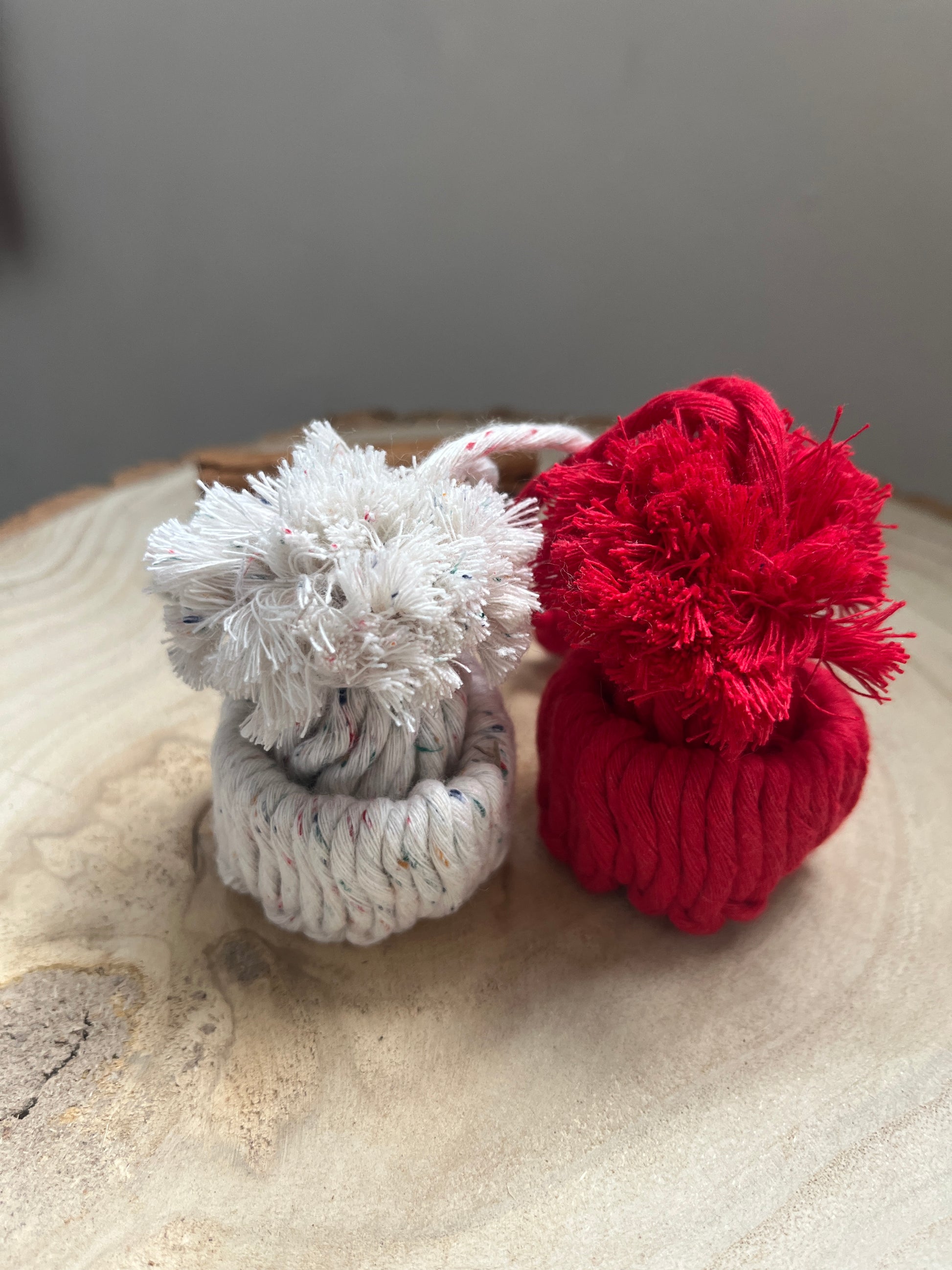 Red and white macrame pom-pom hat ornaments on a textured surface