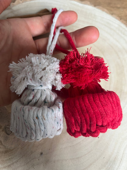 Red and white pom-pom hat ornaments held by a hand against a neutral background
