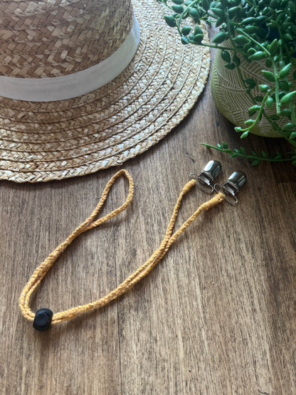 Straw hat on a wooden surface with a yellow chin strap placed next to it. 