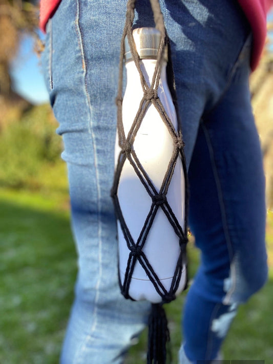 A close up image of a white metal drinking bottle, held securely inside a black yarn holder, which appears to be clipped on to a persons jeans at the hip. 