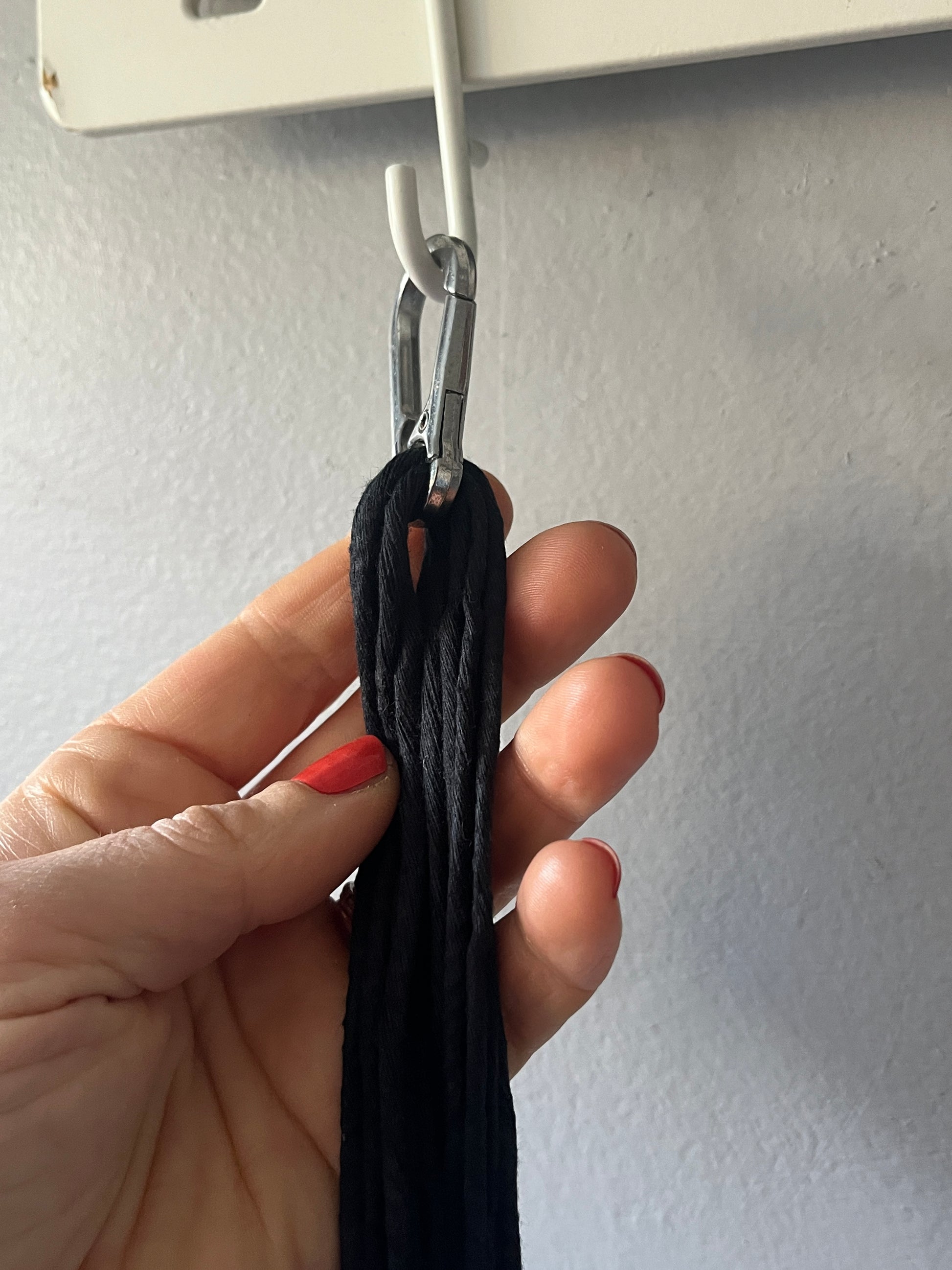 Hand holding a black rope with a silver carabiner against a grey background
