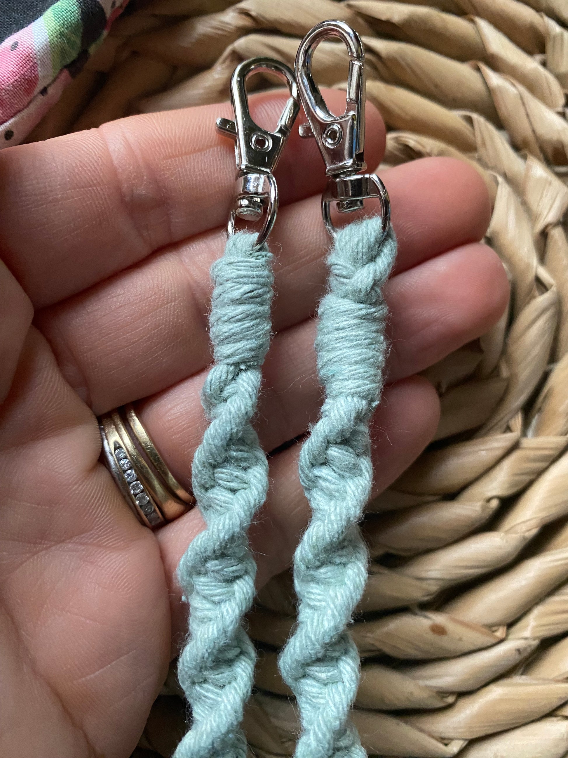 A hand holding the metal clasps on the end of a macramé face mask lanyard made with pastel green cotton cord. 