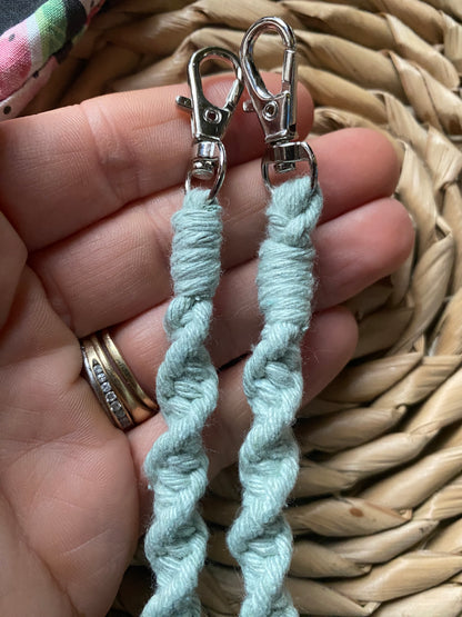 A hand holding the metal clasps on the end of a macramé face mask lanyard made with pastel green cotton cord. 