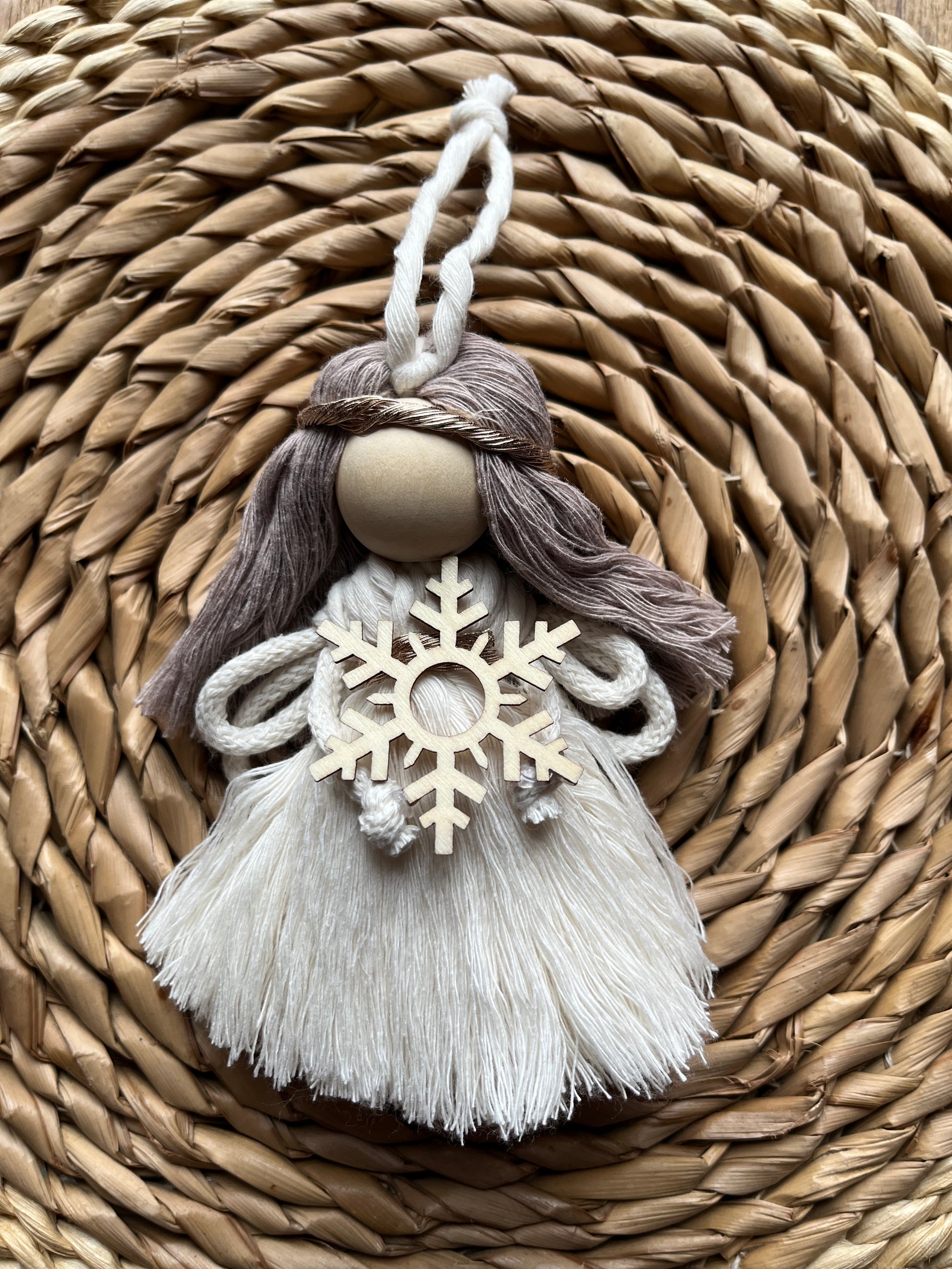 Decorative macrame fairy with tasseled dress and a wooden snowflake, on a woven surface