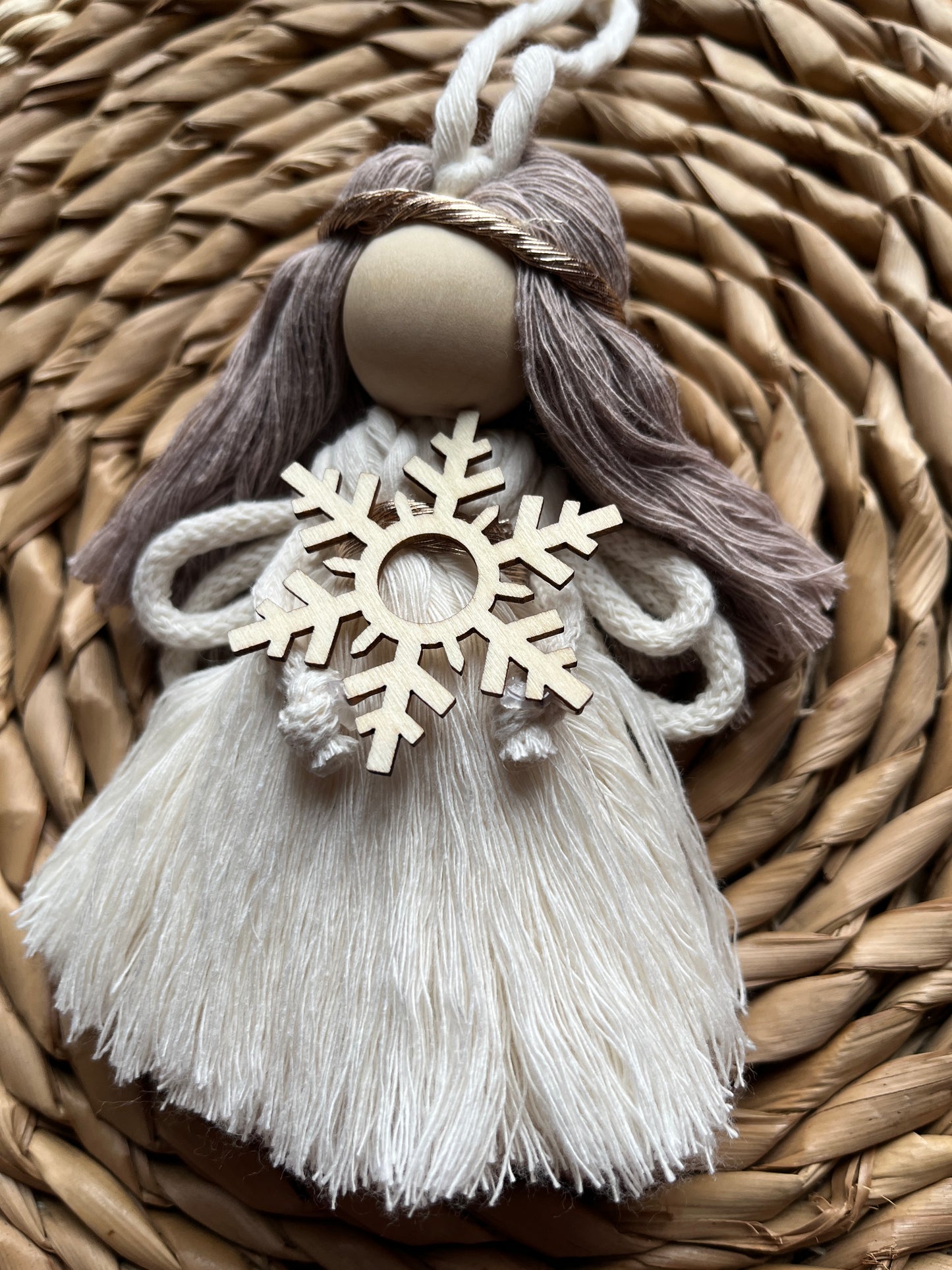 Close up of a decorative macrame fairy with tasseled yarn dress and a wooden snowflake, on a woven surface