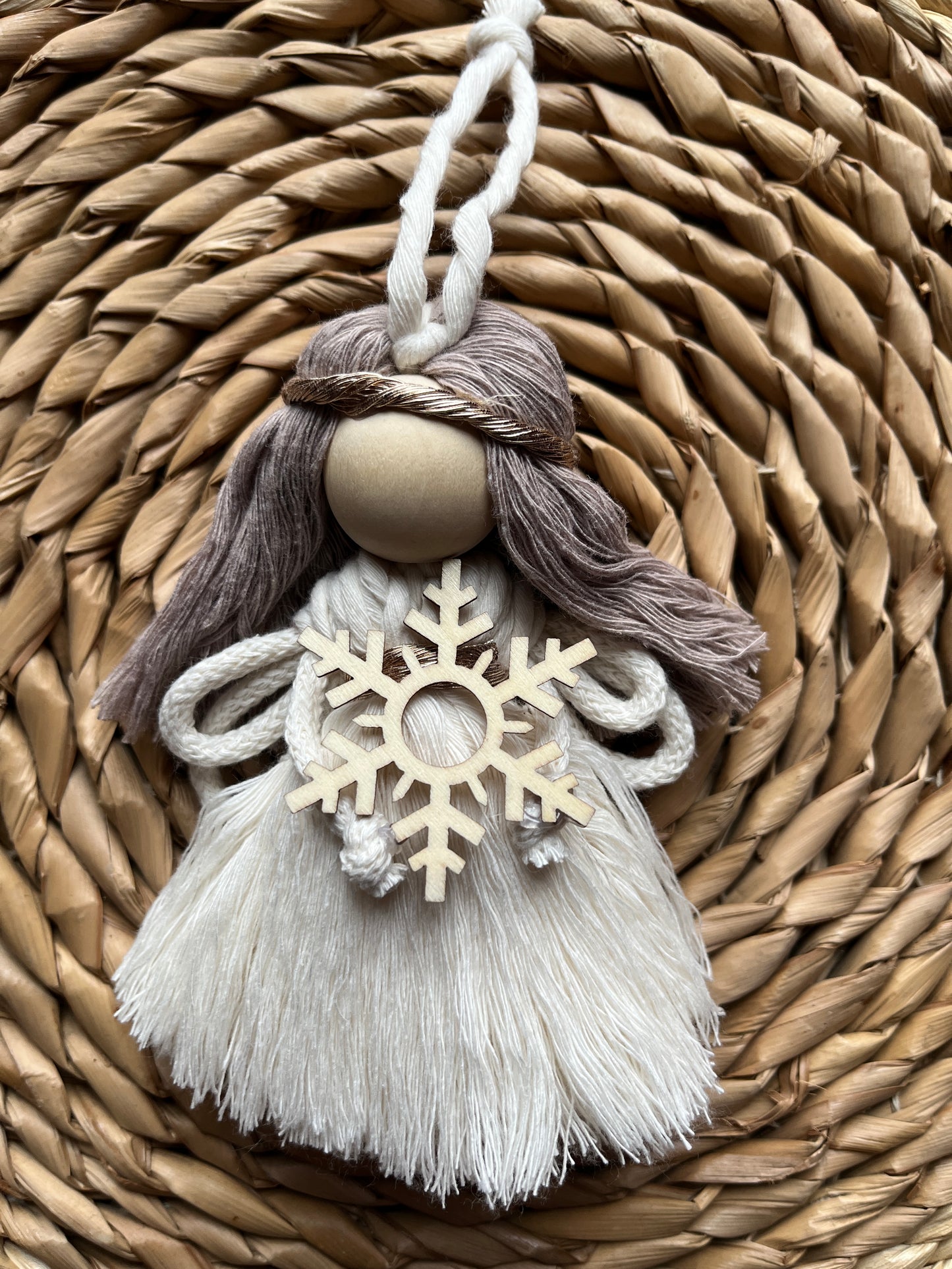 Decorative macrame fairy with tasseled dress and a wooden snowflake, on a woven surface