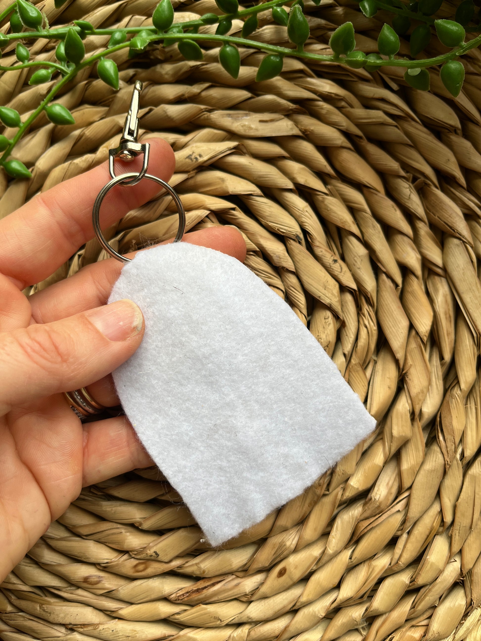 A hand holding a white keychain with silver clasp, showing the reverse side which is covered with white felt. 