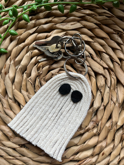 White ghost-shaped keychain with black eyes, attached to a small set of silver keys, on a woven surface