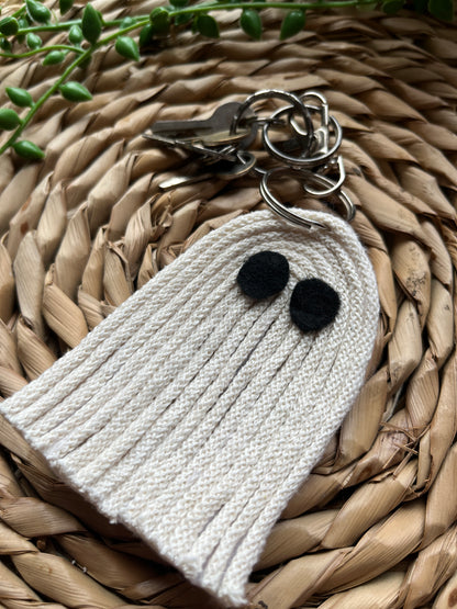 Close up of a white ghost-shaped keychain with black dot eyes on a woven surface