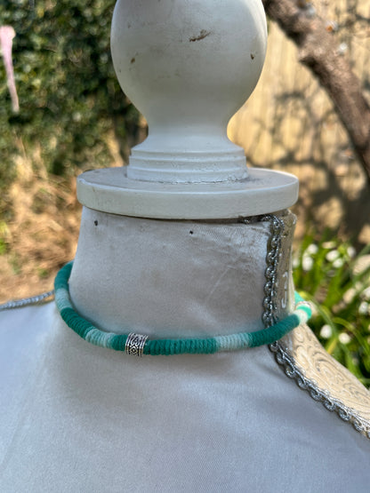 Handmade macrame surfer style short boho necklace, handmade using eco friendly green variegated yarn, and 3 Celtic style spacer beads. Displayed on a white mannequin, outside in the sunshine. 